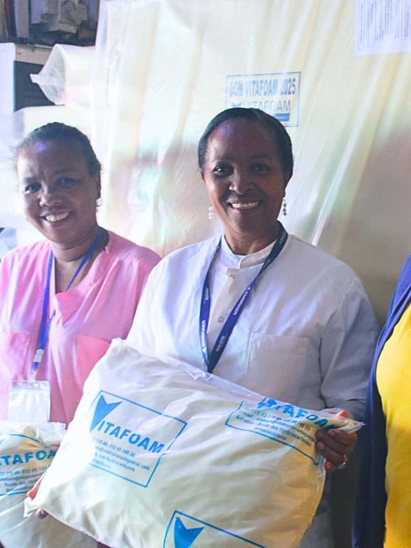 Deux employées Vitafoam en uniformes présentant matelas emballé, kidoro haute densité Madagascar
